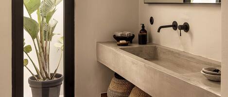 A bathroom with a large window, a potted plant, a sink, and a mirror.