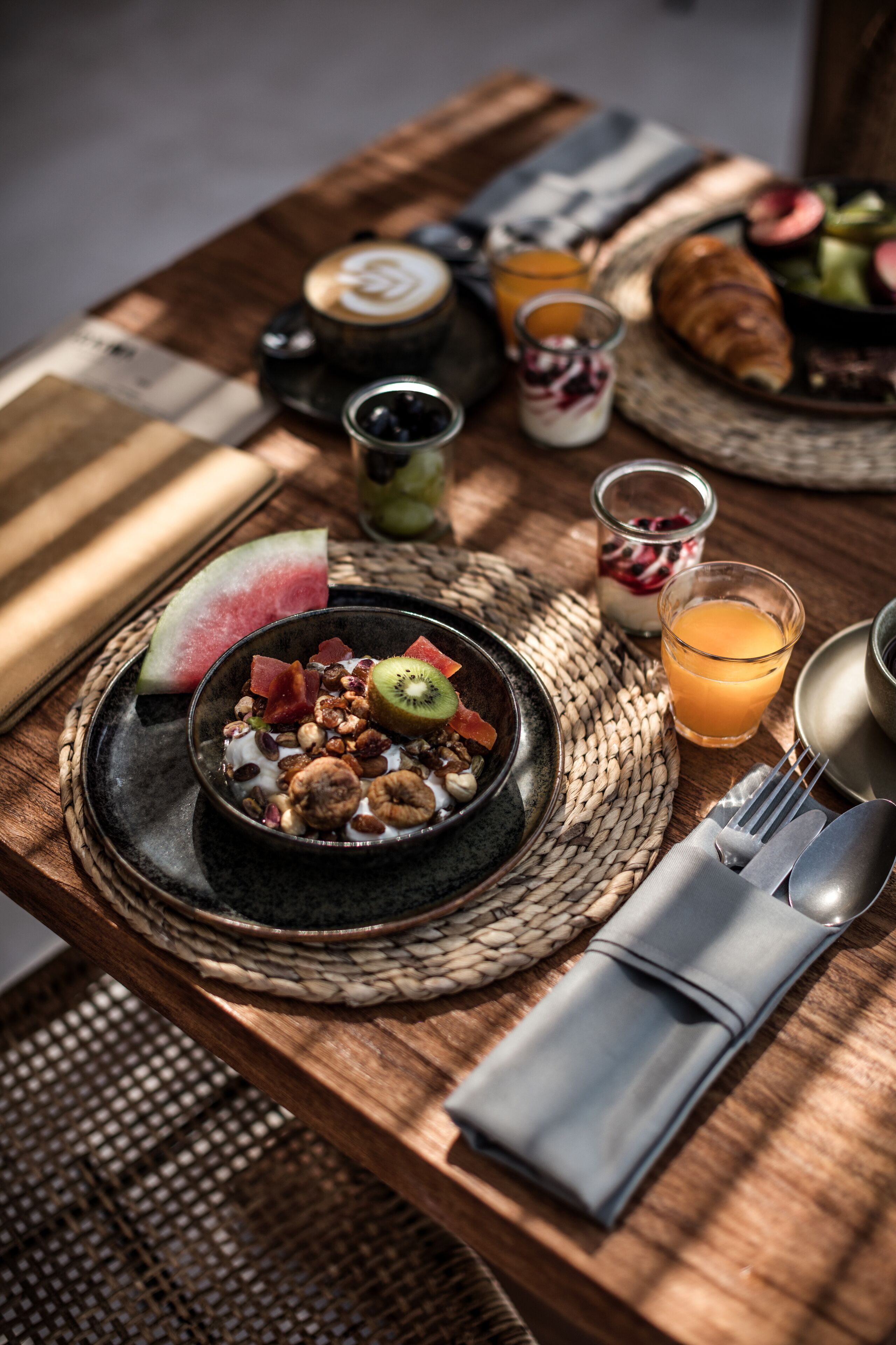 A breakfast setting with a bowl of cereal, a glass of orange juice, and a croissant on a wooden table.