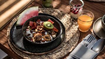 A breakfast setting with a bowl of cereal, a glass of orange juice, and a croissant on a wooden table.