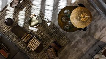 A spacious room with a large window, a round table with a woven lamp, and a patterned rug.