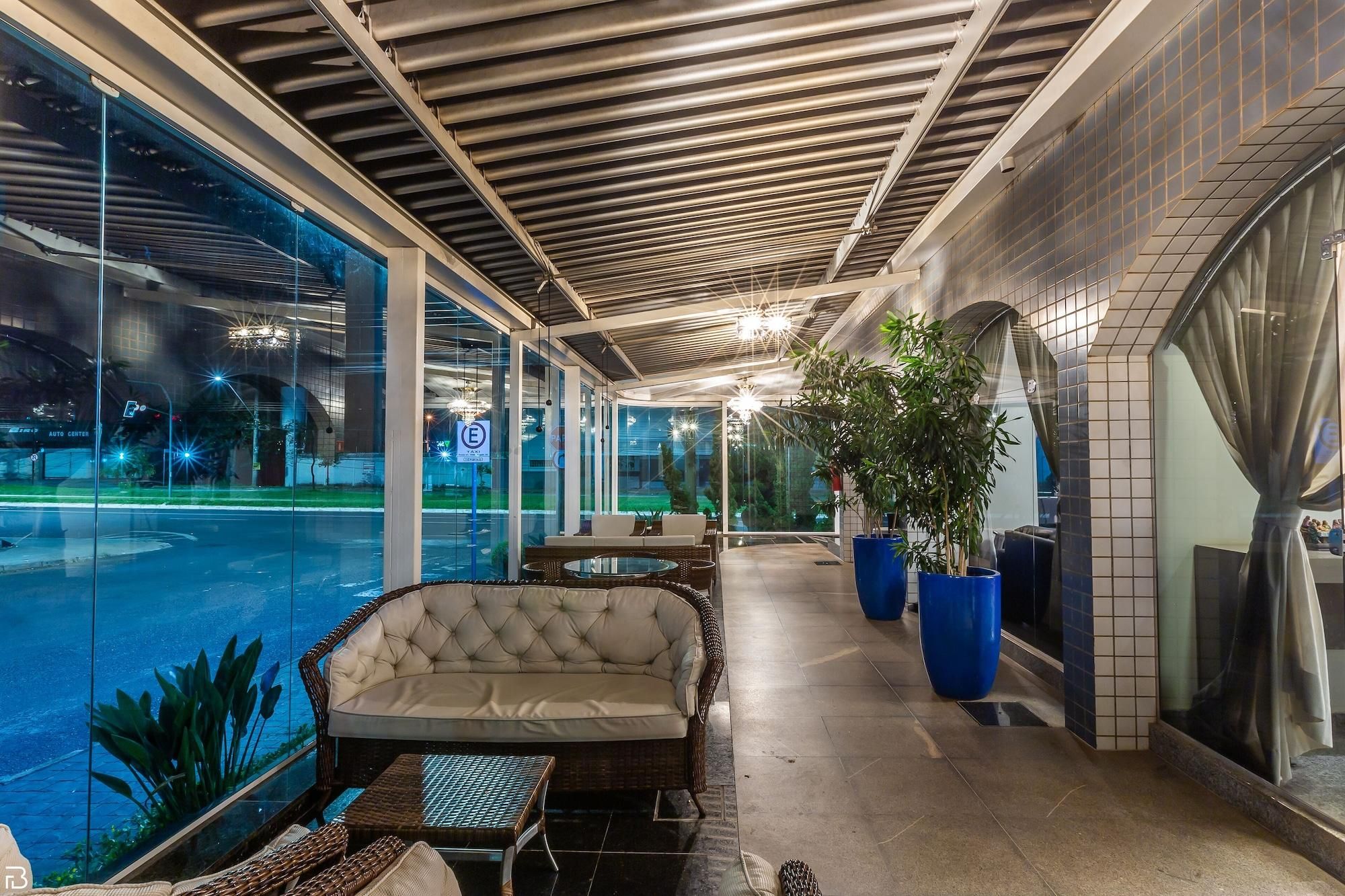 Área de estar coberta ao ar livre com vista para a piscina, com móveis de vime e plantas em vasos.