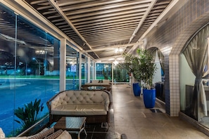 Un espacio de estar al aire libre cubierto con vista a la piscina, con mobiliario de mimbre y plantas en macetas.