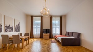 Una sala moderna con suelo de parqué, una mesa de comedor con sillas, un sofá, un mueble para TV y una araña.