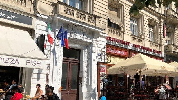 Una calle con mesas al aire libre frente a un restaurante, una pizzería y un edificio con un cartel que dice 'CERRADO'.