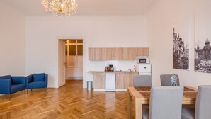 Una sala de estar moderna con piso de madera en patrón de espiga, un comedor con mesa de madera y sillas grises, una cocina con armarios de madera y electrodomésticos blancos, y un candelabro.