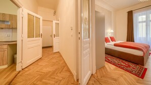 Habitación de hotel con suelo de madera en patrón de espiga, cama con ropa de cama roja, alfombra roja y beige, y un candelabro.