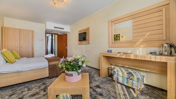 A hotel room with a bed, a small table with a flower vase, a desk with a mirror, and a sofa.