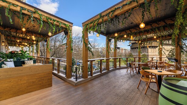 Une terrasse extérieure avec des tables et des chaises en bois, un banc en bois et des guirlandes lumineuses.