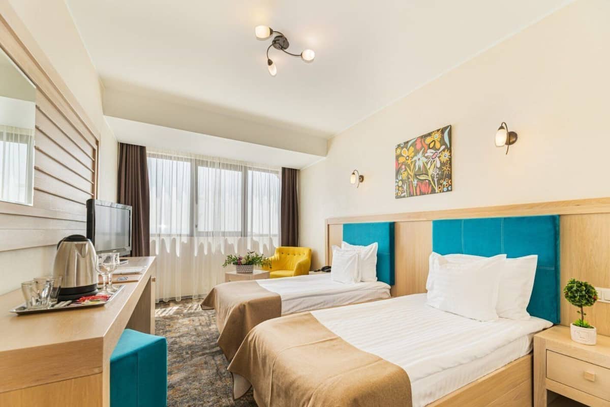 A hotel room with two beds, a desk with a TV, a coffee maker, and a window with curtains.