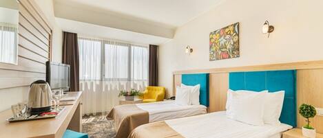 Una habitación de hotel con dos camas, un escritorio con televisor, cafetera y ventana con cortinas.