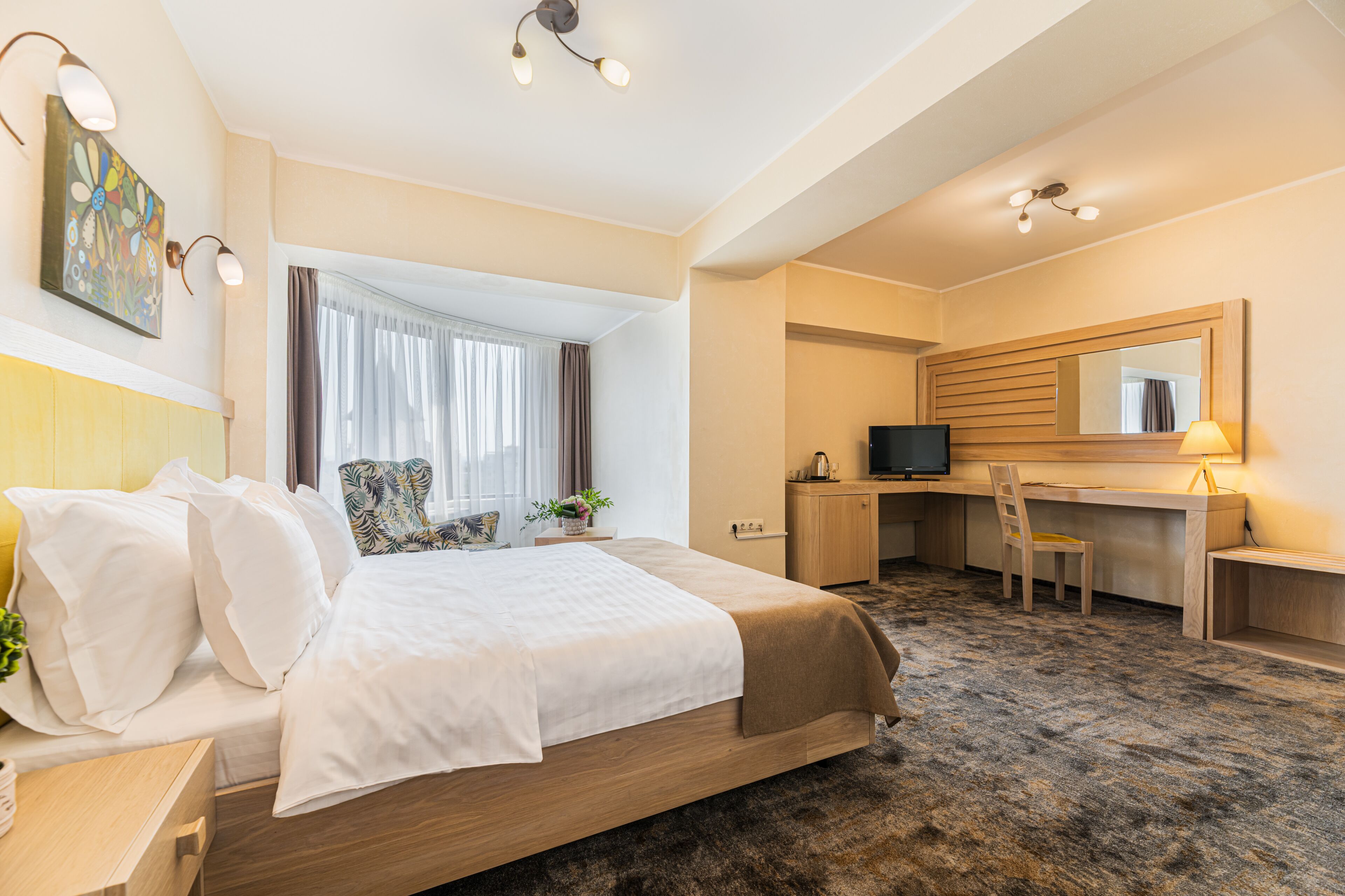 A hotel room with a bed, desk, chair, and a large window with curtains.