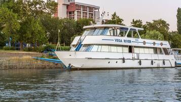 A white boat named "VEGA RIVER" docked near a park with playgrounds and trees.