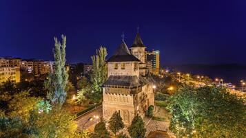 A historic building with a prominent tower, surrounded by trees and modern buildings in the background.