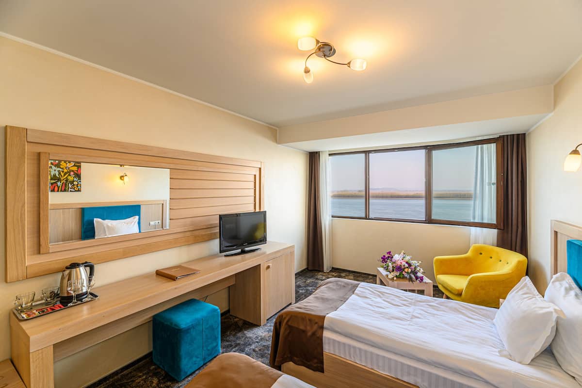 A hotel room with a bed, a desk with a television, a chair, and a large window with a view.
