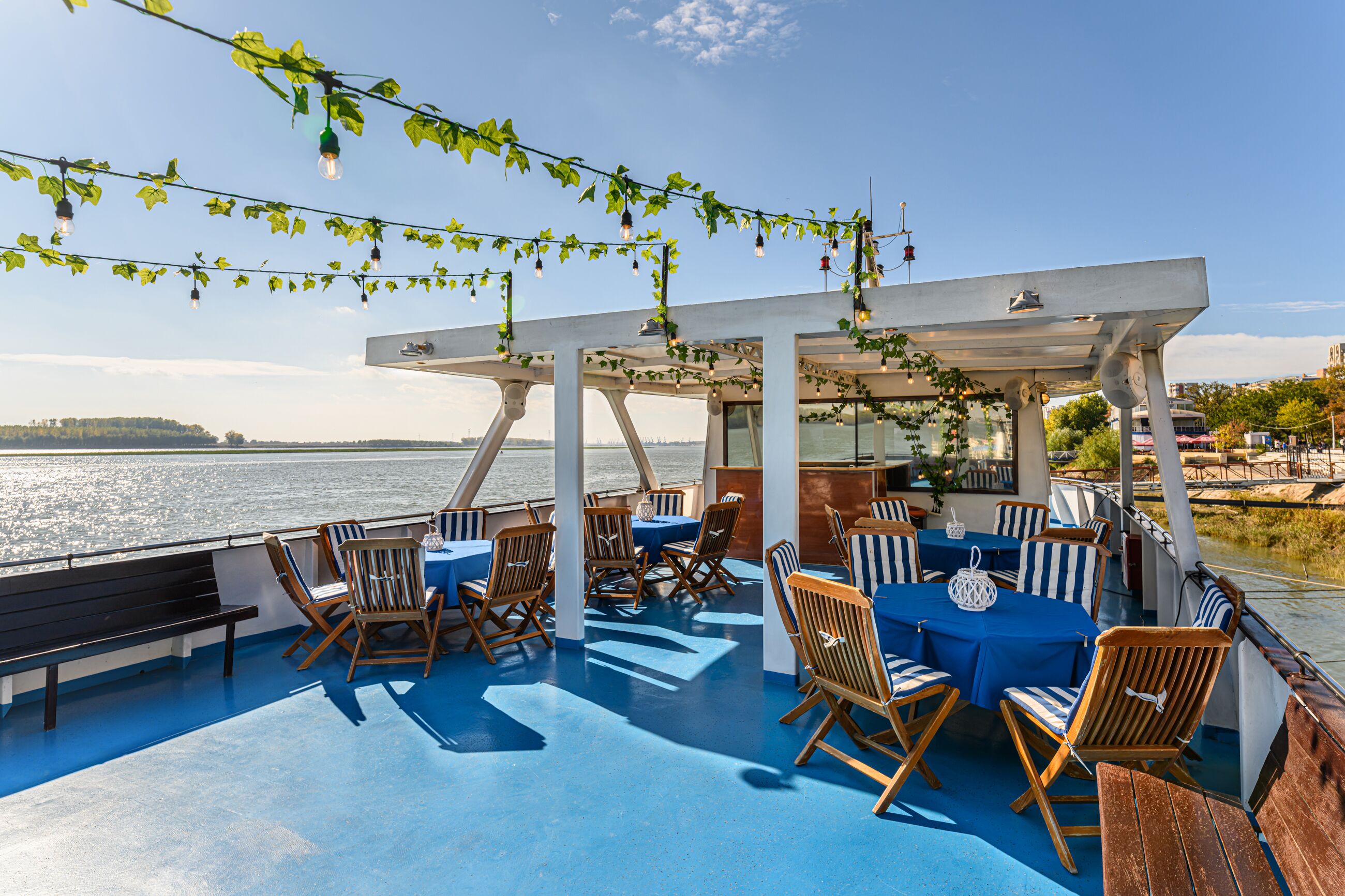 A covered outdoor seating area with tables and chairs, overlooking a body of water.