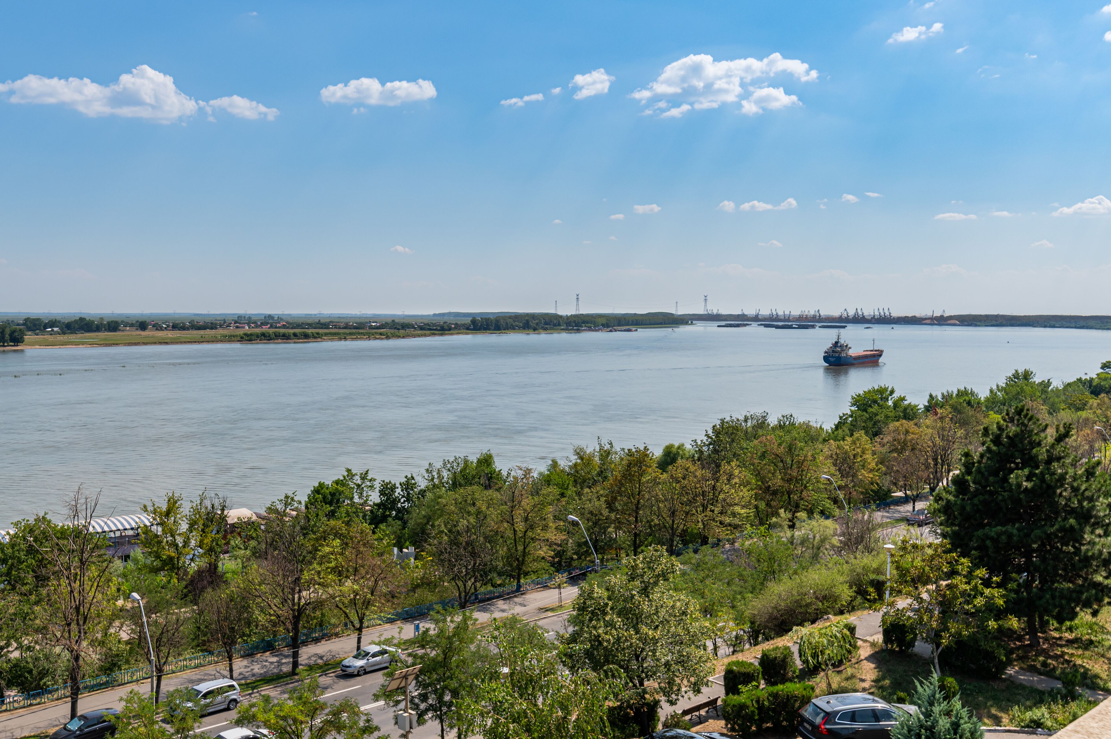 A view of a river with a boat, surrounded by greenery and a clear sky.
