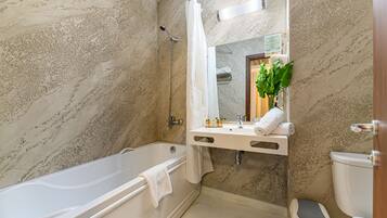 A bathroom with a marble wall, a bathtub, a toilet, and a sink with a mirror above it.