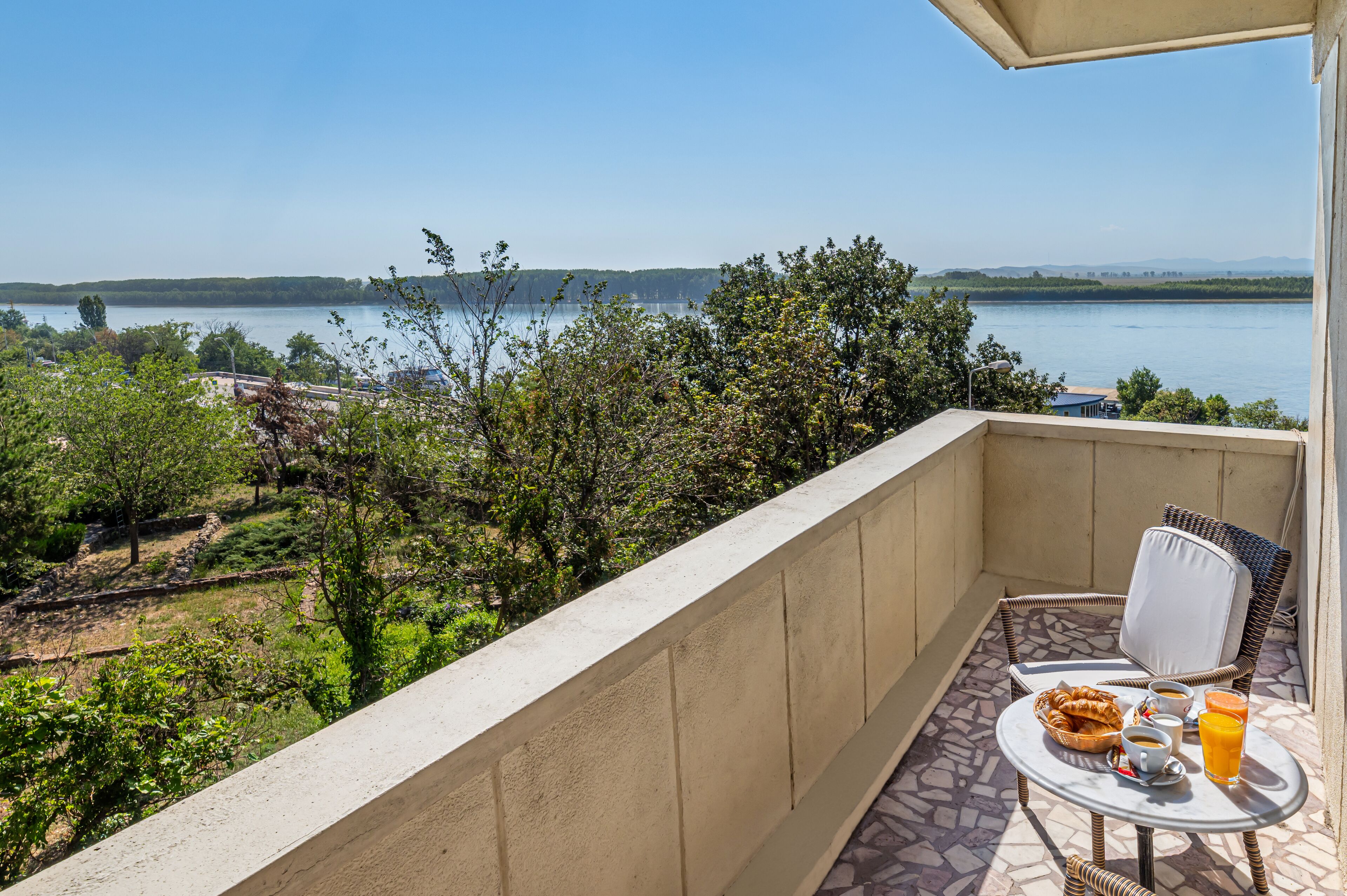 Un balcón con una mesa lista para el desayuno, con vistas a un lago y vegetación.