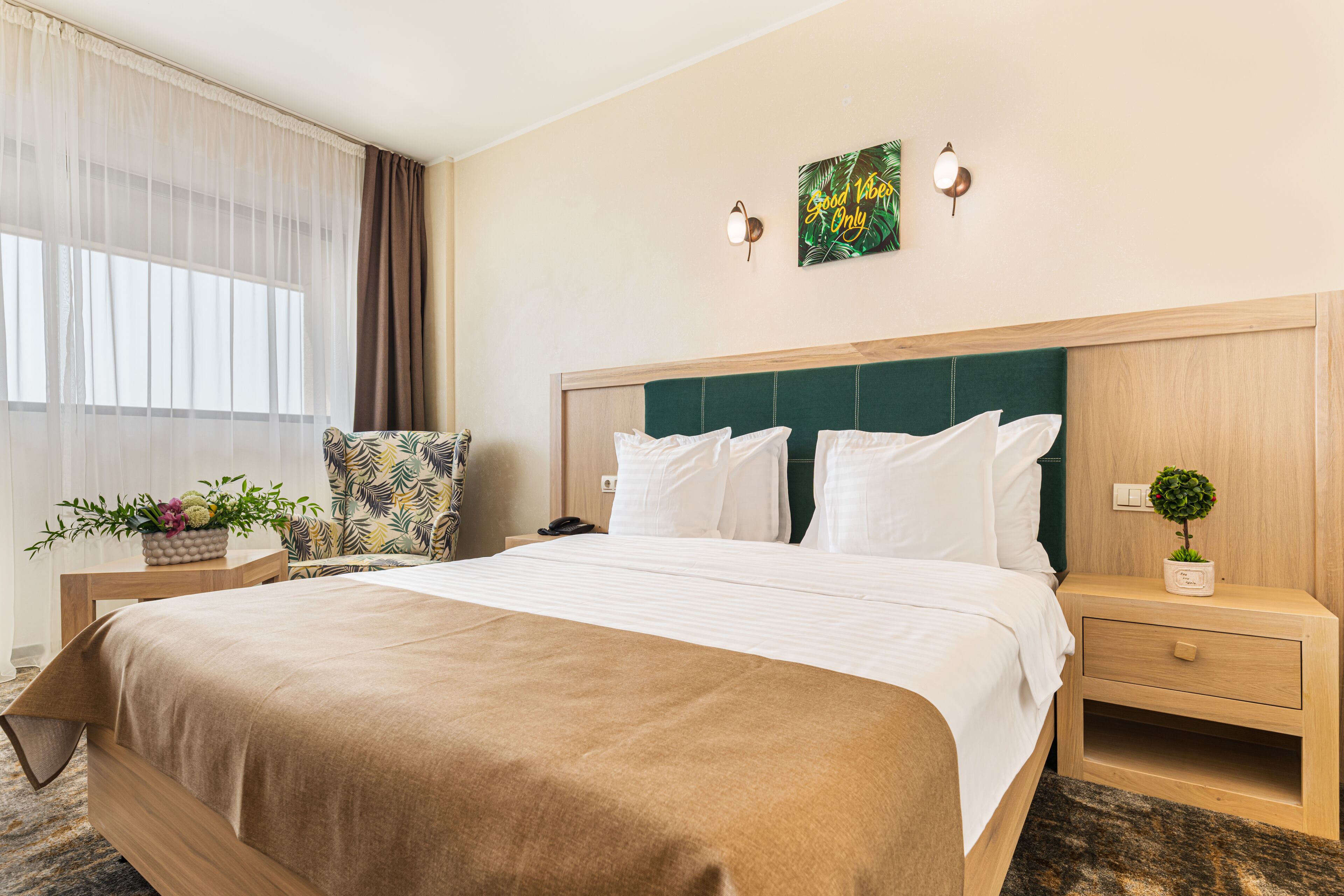 A hotel room with a large bed, a wooden headboard, a nightstand with a plant, and a chair.