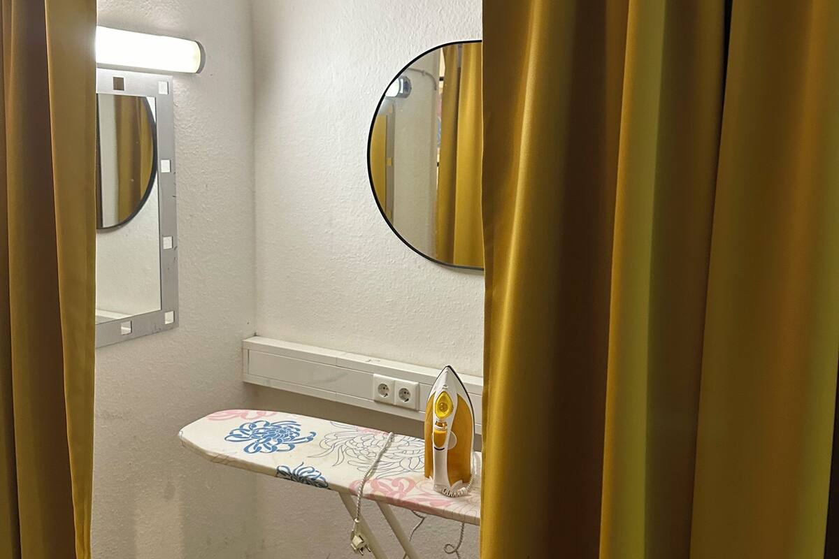 A bathroom with a mirror, a small shelf with toiletries, and a shower curtain.