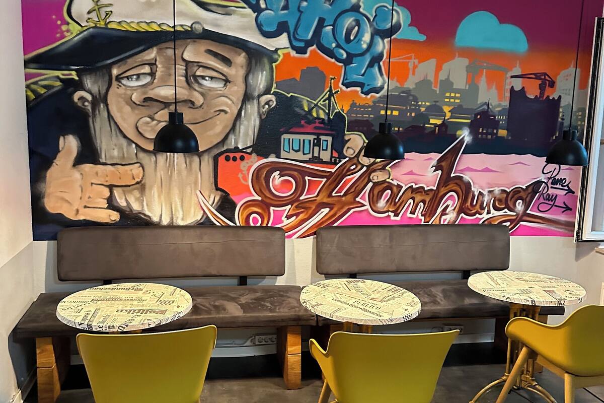 A seating area with a mural, tables with newspaper-patterned placemats, and yellow chairs.