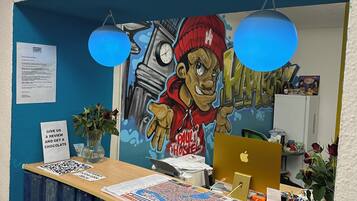 Un mostrador de recepción con un mural, un reloj y un cartel que indica la zona de recepción.