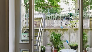 Puerta abierta que da a un patio exterior con escalera de metal, plantas en macetas y mobiliario de exterior.