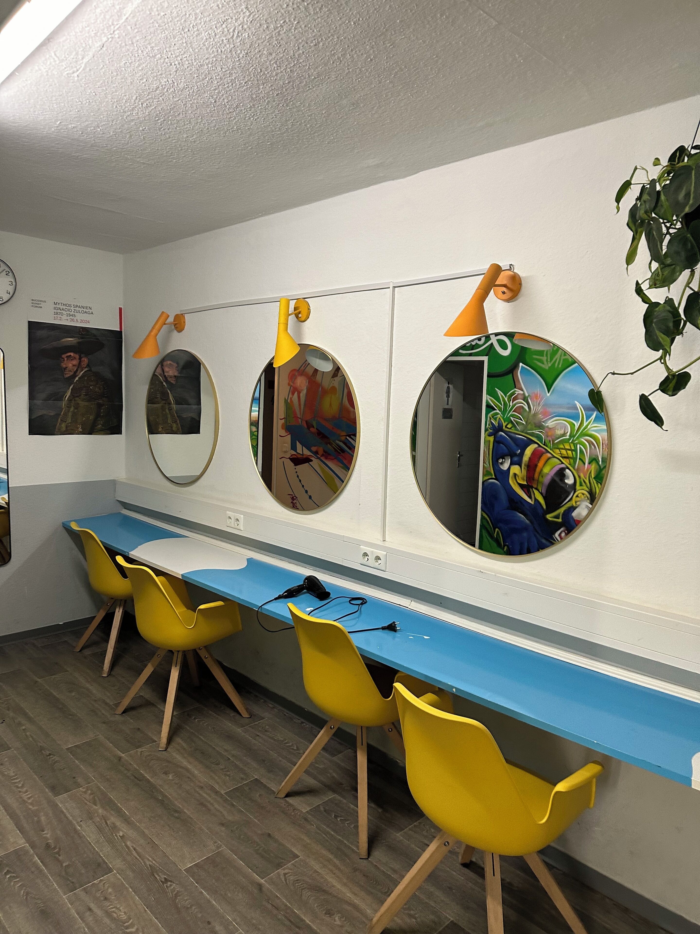 A room with a long blue table, yellow chairs, and three round mirrors with different artworks.