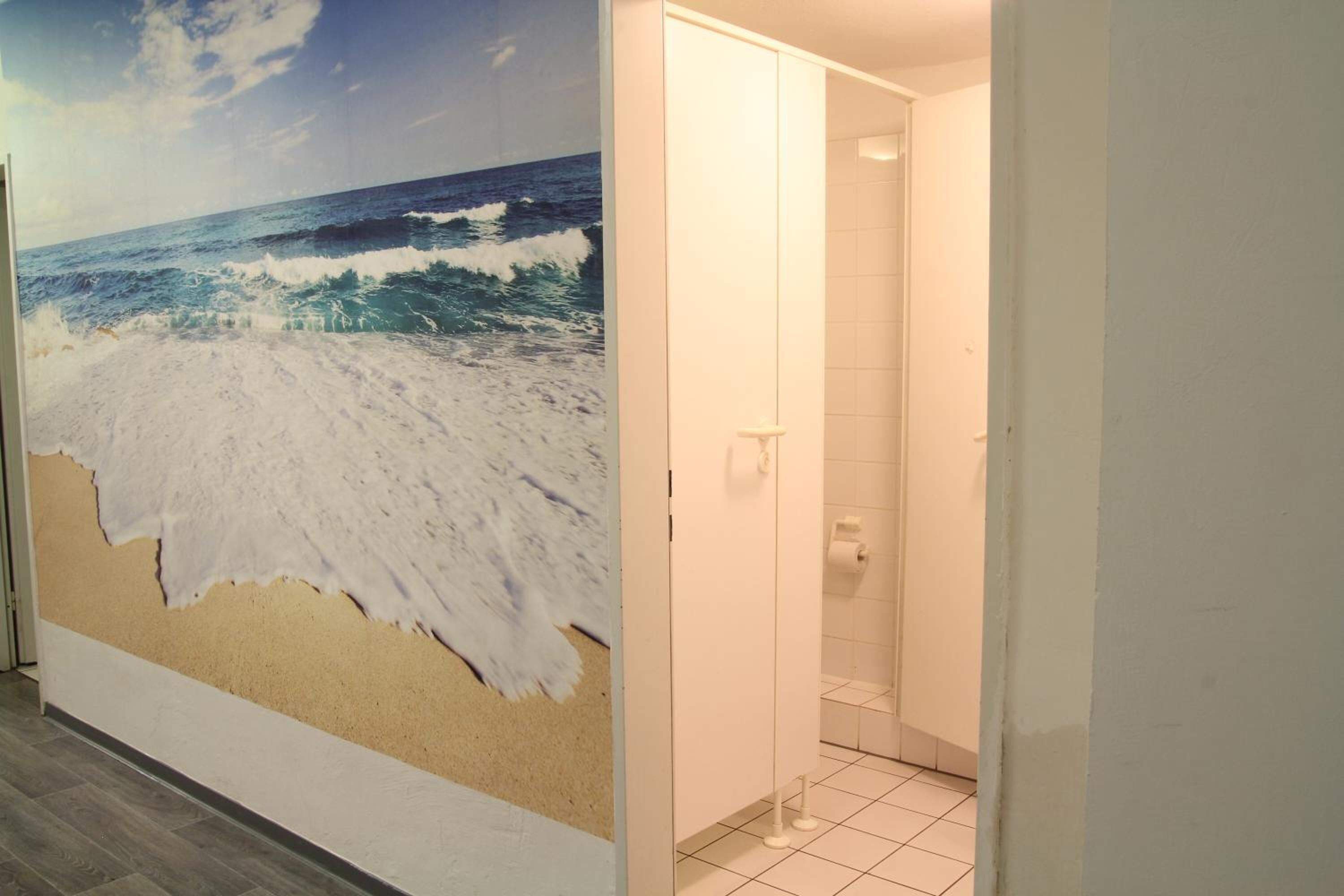 Casa de banho com um grande mural na parede retratando uma cena de praia, uma porta branca e chão em azulejos.