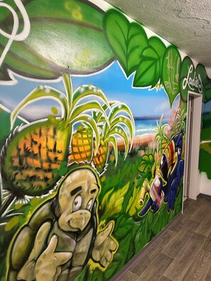 A mural with a tropical theme, including a frog, a pineapple, and a cartoon character. - Pauli Hostel (Hamburg)