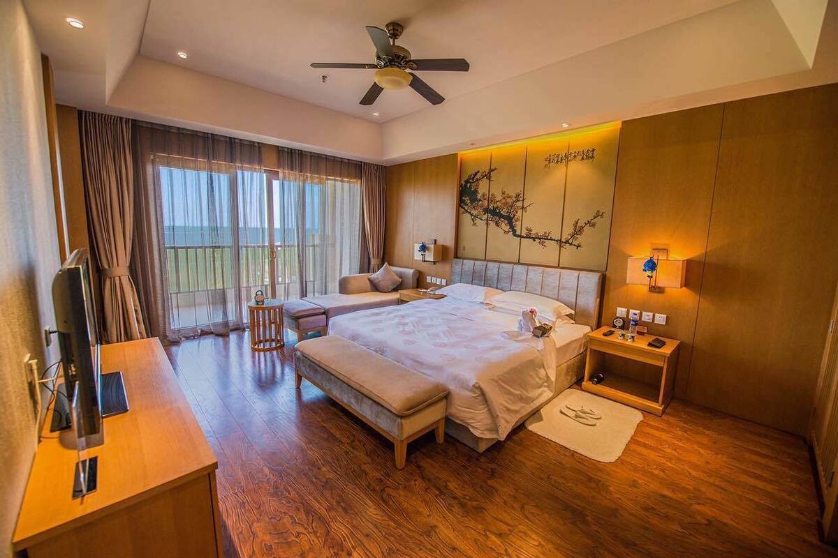 A spacious bedroom with a large bed, a desk, and a balcony.