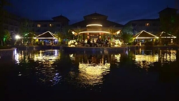 A nighttime view of a hotel with a central building and two illuminated structures on either side, reflecting on a body of water. - Arcadia seaside holiday hotel Beidaihe (Qinhuangdao)