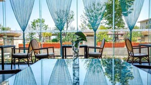 An outdoor seating area with a glass table and chairs, surrounded by blue fabric structures and greenery. - Arcadia seaside holiday hotel Beidaihe (Qinhuangdao)