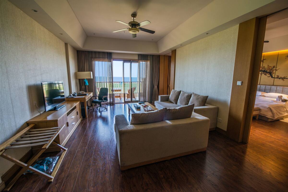 A hotel room with a sofa, a TV, a desk, a chair, and a balcony with a view.