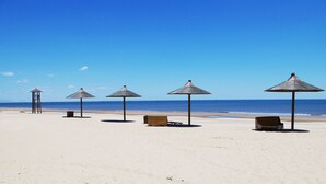 A beach with five thatched umbrellas and wooden benches, a clear sky, and the ocean in the background. - Arcadia seaside holiday hotel Beidaihe (Qinhuangdao)