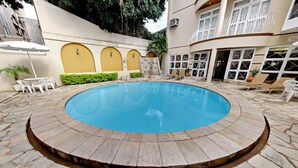 A circular pool with a stone border, surrounded by lounge chairs and a small table. - Tamareiras Park Hotel (Uberaba)