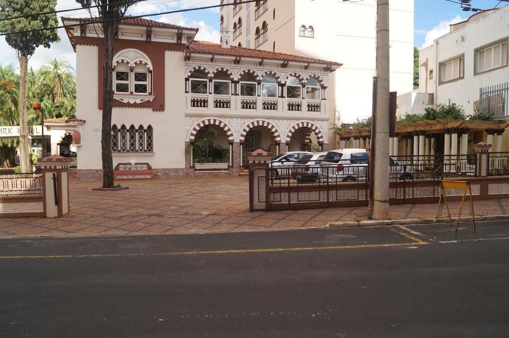 Un edificio con entrada de baldosas, zona de estacionamiento con portón y letrero visible de un hotel.