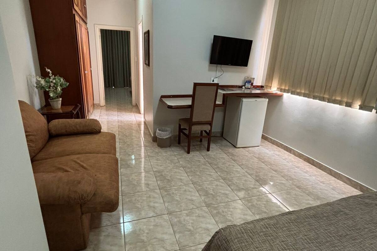 A hotel room with a bed, a sofa, a desk with a chair, a television, and a window with blinds.
