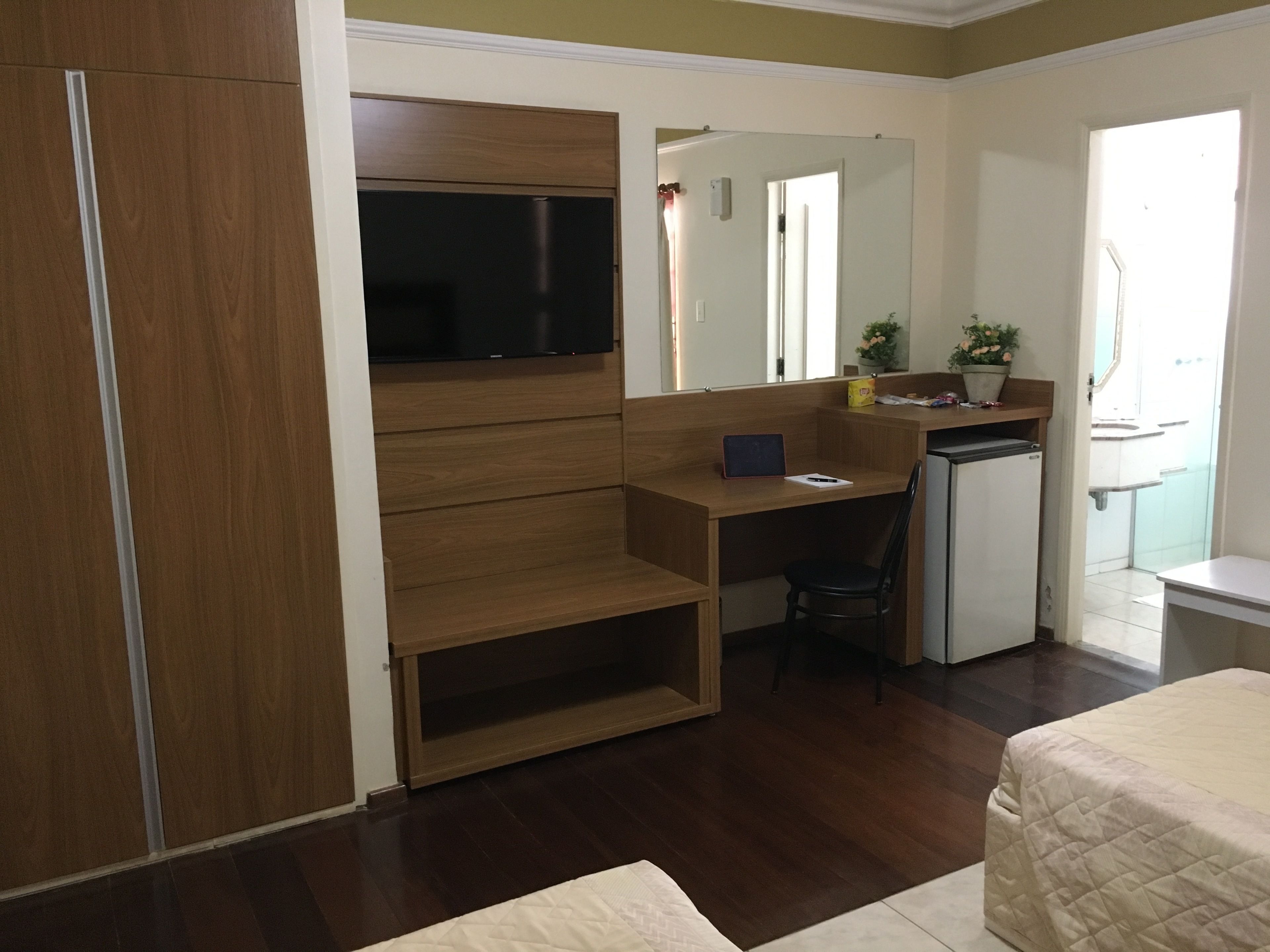 A compact room with a bed, a desk, a chair, a small kitchenette, and a TV.