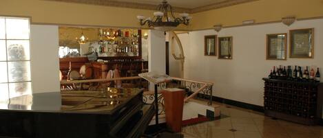 A spacious room with a grand piano, a staircase, a bar area, and a wine rack.