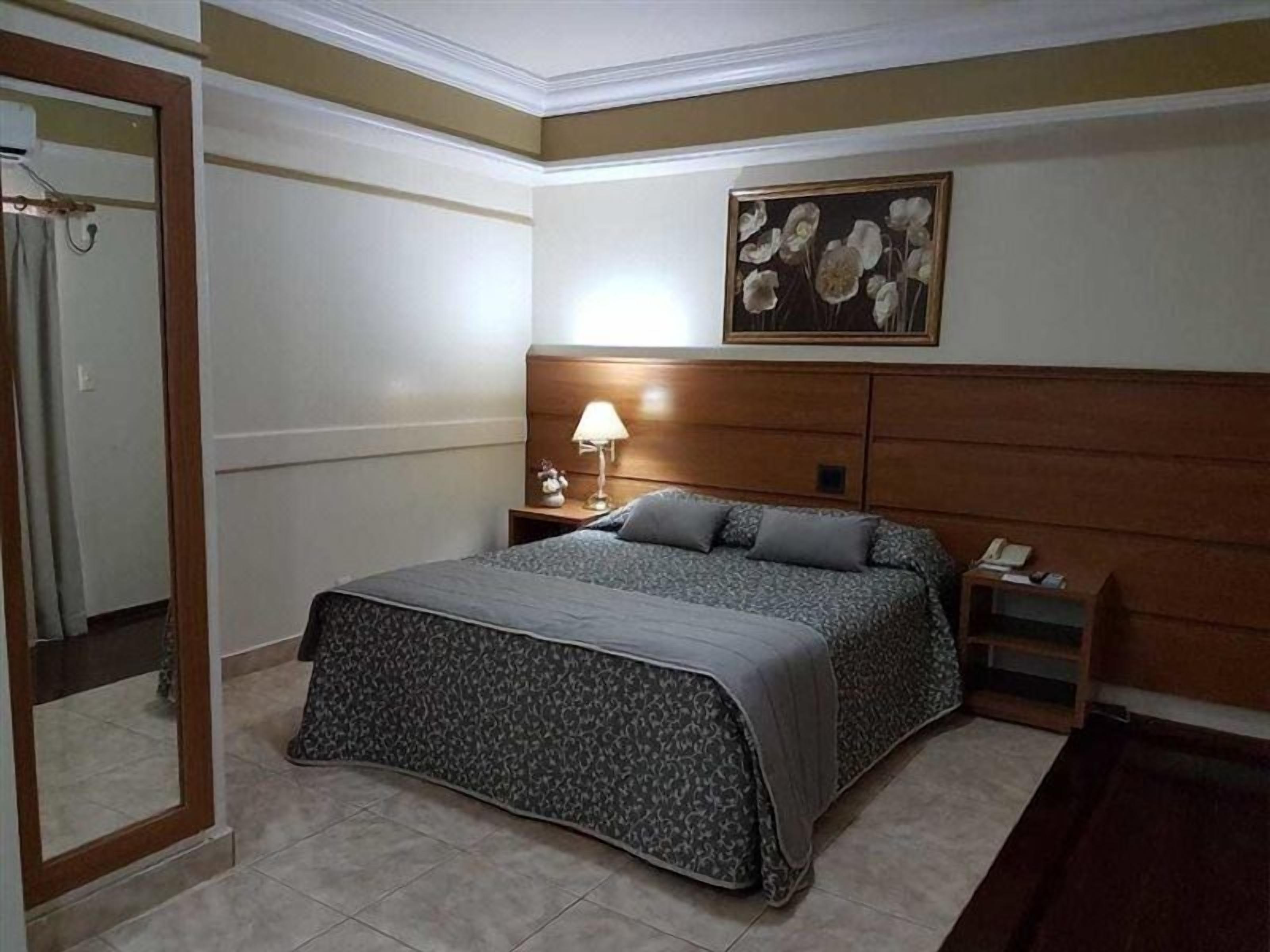 A bedroom with a bed, a nightstand, a lamp, a painting, and a mirror.