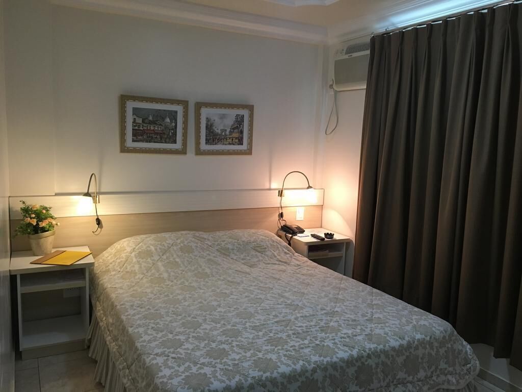 A hotel room with a bed, bedside tables, a lamp, a phone, and a wall-mounted air conditioner.