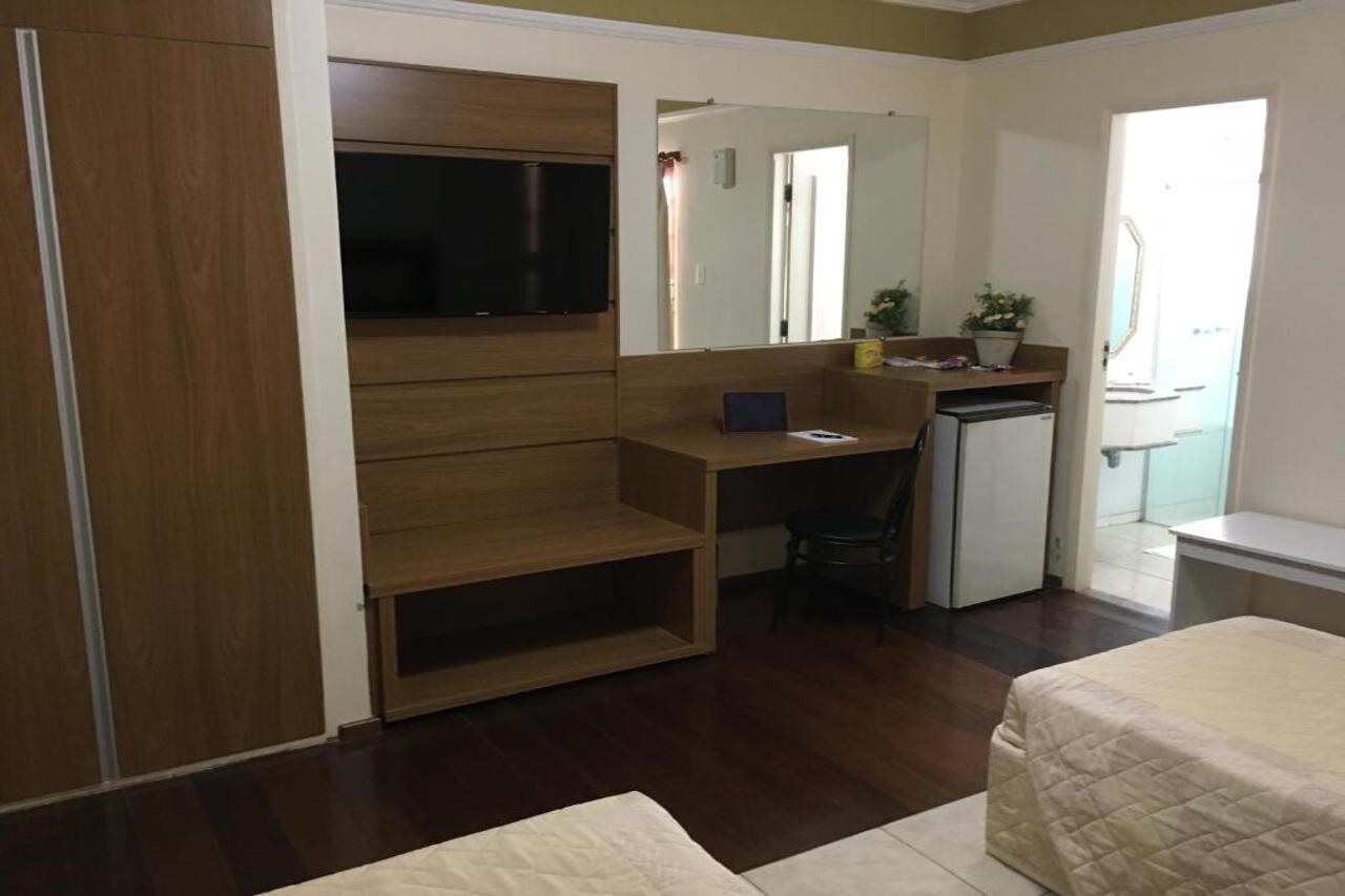 A compact room with a bed, a desk, a chair, a TV, and a small refrigerator.