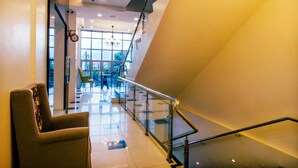 Een moderne hotel lobby met een trap, een zithoek en grote ramen die natuurlijk licht binnenlaten.