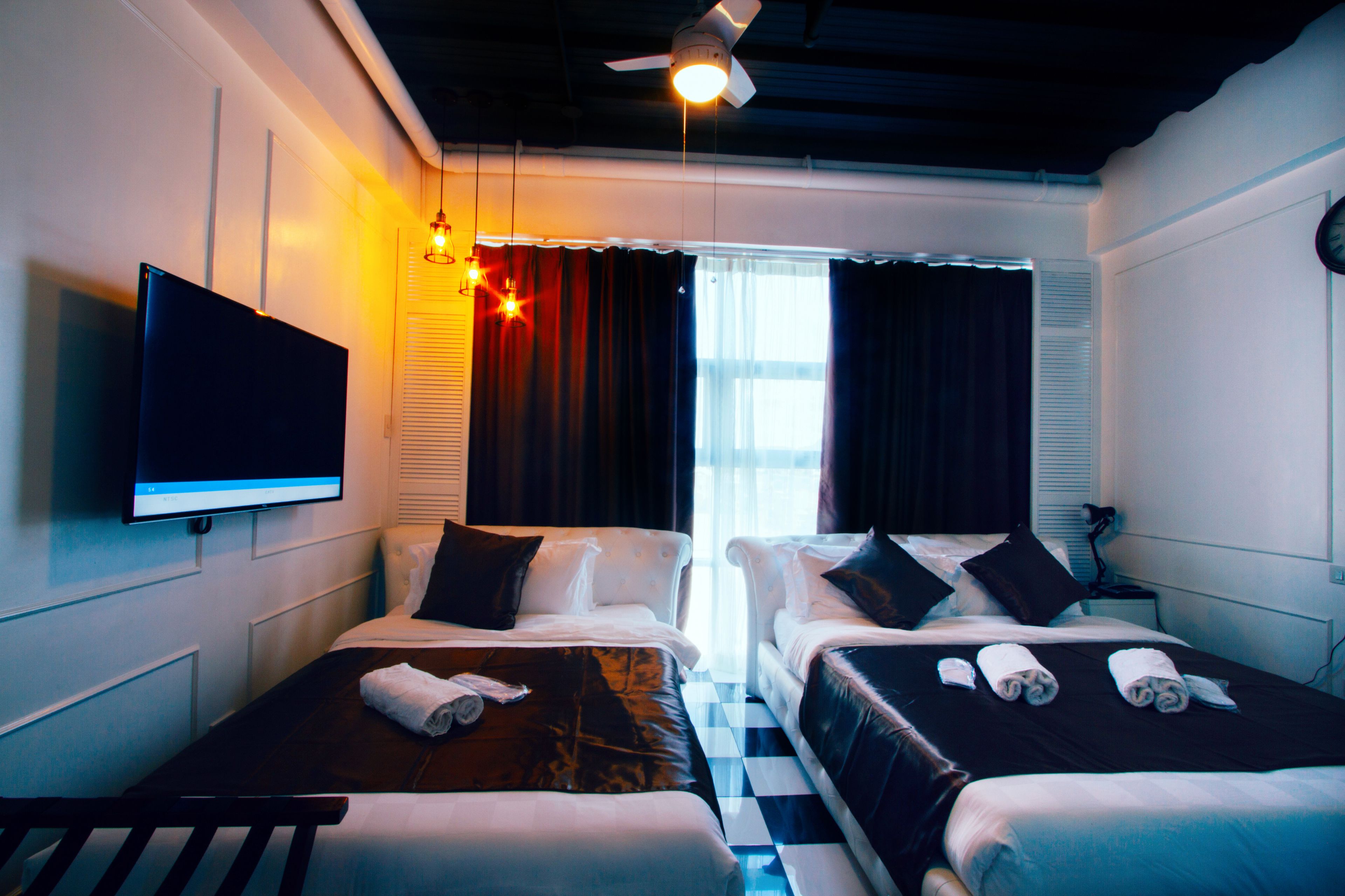A hotel room with two beds, a flat-screen TV, a ceiling fan, and a window with curtains.
