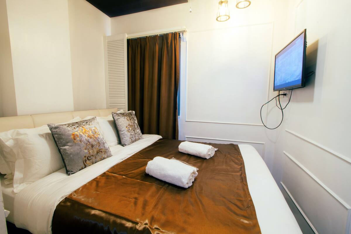 Ein Hotelzimmer mit einem Bett, Kissen, einem Fernseher und einem Fenster mit Vorhängen.