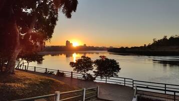 A sunset view over a calm river with a park area and a bridge.