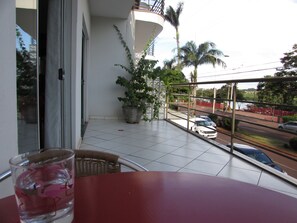 A balcony with a potted plant, a glass of water, and a view of the street.