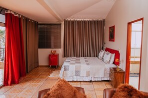 A bedroom with a bed, curtains, a window with blinds, a red cabinet, and a wooden nightstand.