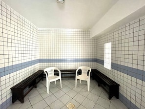 Un baño con baldosas, dos sillas de plástico blanco y un banco.